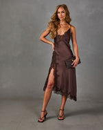 Brown satin midi slip dress with lace trim and thigh-high slit, styled with strappy heeled sandals and a brown clutch