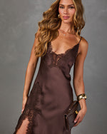 Woman in a chocolate brown satin slip dress with lace trim and side slit, styled with gold cuff bracelet and leather clutch