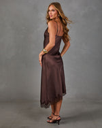 Woman in a brown satin midi slip dress with lace hem, gold cuff bracelet and strappy heels, looking over her shoulder