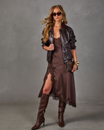 Woman in brown satin lace-trim slip dress, chocolate faux leather bomber jacket, knee-high boots, sunglasses and gold bracelets