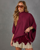 Woman wearing a burgundy knit turtleneck poncho sweater with crushed velvet shorts trimmed in cream lace and gold cuff bracelets