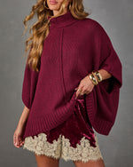 Burgundy knit turtleneck poncho sweater with ribbed hem, styled with crushed velvet shorts with cream lace trim and gold cuffs