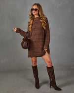 A woman models a brown chunky knit sweater dress with matching brown suede knee-high boots, sunglasses, and a small brown handbag against a gray studio backdrop.
