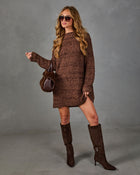 A woman models a brown chunky knit sweater dress with matching brown suede knee-high boots, sunglasses, and a small brown handbag against a gray studio backdrop.