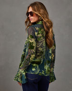 Woman in sheer green floral devoré blouse with bell sleeves and velvet collar, styled with aviator sunglasses and dark jeans