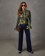 Sheer green floral bow-neck blouse with flared sleeves, styled with dark wide-leg jeans, brown woven clutch and pointed heels