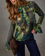 Sheer green floral burnout velvet blouse with pussy bow neck and bell sleeves, styled with dark wide-leg jeans and woven clutch