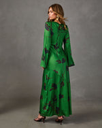 Green satin maxi dress with floral print, bell sleeves and tie-back neckline, styled with gold earrings and strappy heels