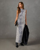 A woman models a sleeveless, high-neck maxi dress with a black and white animal print pattern, holding a black faux fur coat and clutch against a textured gray studio backdrop.