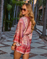 Woman in boho floral print romper with long sleeves, gold accessories, and aviator sunglasses on a cobblestone street