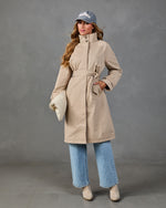 Woman wearing belted beige trench coat, wide-leg jeans, nude heeled sandals, and gray Hamptons baseball cap