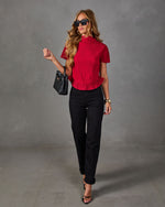 Woman in a red pleated mock-neck peplum top, black straight-leg jeans, strappy heels, sunglasses and black woven handbag