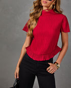 Red pleated mock neck short sleeve top with ruffle hem, styled with black high-waisted pants, gold hoops and bangles
