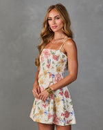Woman wearing white floral mini dress with spaghetti straps, pink and yellow flowers, fitted bodice, flared skirt, gold jewelry