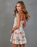 Woman modeling cream floral mini dress with spaghetti straps, open back, and A-line skirt, styled with gold bangles