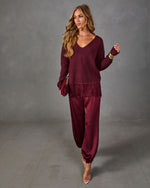 Woman in a burgundy V-neck sweater with lace hem, satin jogger pants, clear heels, gold bracelets and a velvet clutch