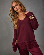 Woman wearing a burgundy V-neck sweater with lace hem, matching satin pants, gold cuff bracelets and a velvet clutch
