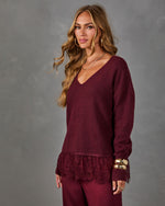 Woman wearing a burgundy V-neck sweater with lace hem and matching wide-leg pants, styled with gold cuffs and layered necklaces