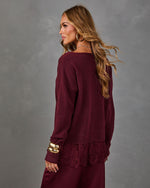 Woman in a burgundy knit sweater with lace hem, gold hoop earrings and chunky bangles, styled with a satin maroon skirt