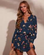 Navy blue floral long sleeve mini dress with V-neck and ruffle hem, worn by blonde woman with gold hoop earrings