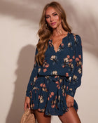 Navy blue floral long sleeve mini dress with V-neck and ruffle hem, worn by blonde woman with gold hoop earrings
