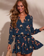 Navy blue floral long-sleeve mini dress with V-neck, tiered ruffle skirt, and smocked cuffs on smiling woman
