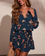 Navy blue floral long sleeve mini dress with V-neckline and ruffle hem, worn by smiling woman with wavy hair