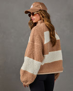 Woman in tan and cream color block sherpa fleece pullover with baseball cap, sunglasses and black leggings, seen from behind
