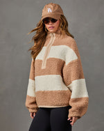 Woman wearing a tan and cream striped sherpa half-zip pullover with black leggings, an LA baseball cap and sunglasses