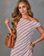 Woman wearing striped off-shoulder dress with tan woven leather bucket bag and gold bangle bracelets, fashion editorial