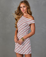 Woman wearing striped one-shoulder mini dress in rose and white diagonal print with ruched side detail and gold bangles