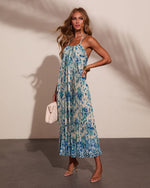 Blue floral pleated halter maxi dress on blonde model with strappy heels and white woven bag