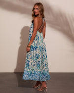 Blue floral print halter maxi dress with open back, pleated skirt, worn with nude heeled sandals and gold bracelets