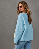 Woman in oversized light blue knit sweater, aviator sunglasses and light-wash jeans, glancing over her shoulder, back view