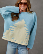 Woman wearing light blue oversized knit sweater with cream pine tree design, aviator sunglasses and light-wash jeans
