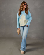 Light blue oversized sweater with cream pine tree design, styled with flare jeans, woven clutch, aviators and platform boots