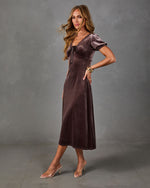 Woman in a brown velvet midi dress with puff sleeves, lace neckline and satin bow, styled with clear-strap nude heels