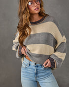Woman wearing an oversized gray and cream striped knit sweater with light-wash wide-leg jeans and tinted aviator glasses
