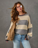 Woman wearing an oversized gray and cream striped knit sweater with light wash jeans, aviator glasses and a tan suede tote bag