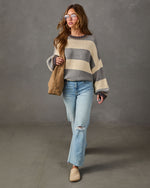 Woman in oversized gray and cream striped sweater, light wash distressed jeans, tan clogs and suede tote bag walking
