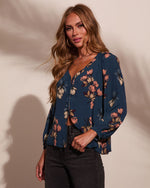 Woman wearing teal floral print long-sleeve blouse with V-neck and button front, paired with dark jeans