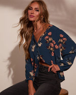 Woman wearing teal floral print long-sleeve wrap crop top with v-neckline, paired with dark gray jeans