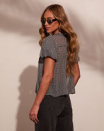 Woman wearing black white gingham check crop top with short sleeves, dark jeans, gold hoop earrings, retro sunglasses