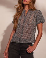 Women's black and white gingham check blouse with short puff sleeves, button front, and smocked neckline, styled with dark jeans