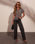 Woman in gingham sheer blouse, dark wide-leg jeans, black kitten heels, holding quilted bag, wearing retro sunglasses