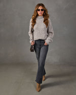 Woman wearing a gray fuzzy mock neck sweater, dark gray flare jeans, tan ankle boots, sunglasses and a brown crossbody bag