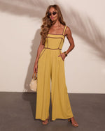 Woman wearing mustard yellow wide-leg jumpsuit with burgundy trim, straw bag, cork heels, and gold accessories