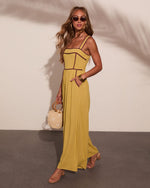 Woman wearing chartreuse maxi dress with burgundy piping, corset bodice, holding straw bag, styled with sandals and sunglasses