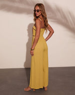Woman modeling yellow-green spaghetti strap wide-leg jumpsuit with contrast trim, gold bangles, strappy heels, and sunglasses