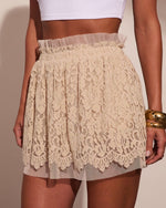 Beige floral lace mini skirt with scalloped hem and tulle underlayer, paired with white crop top and gold cuff bracelet